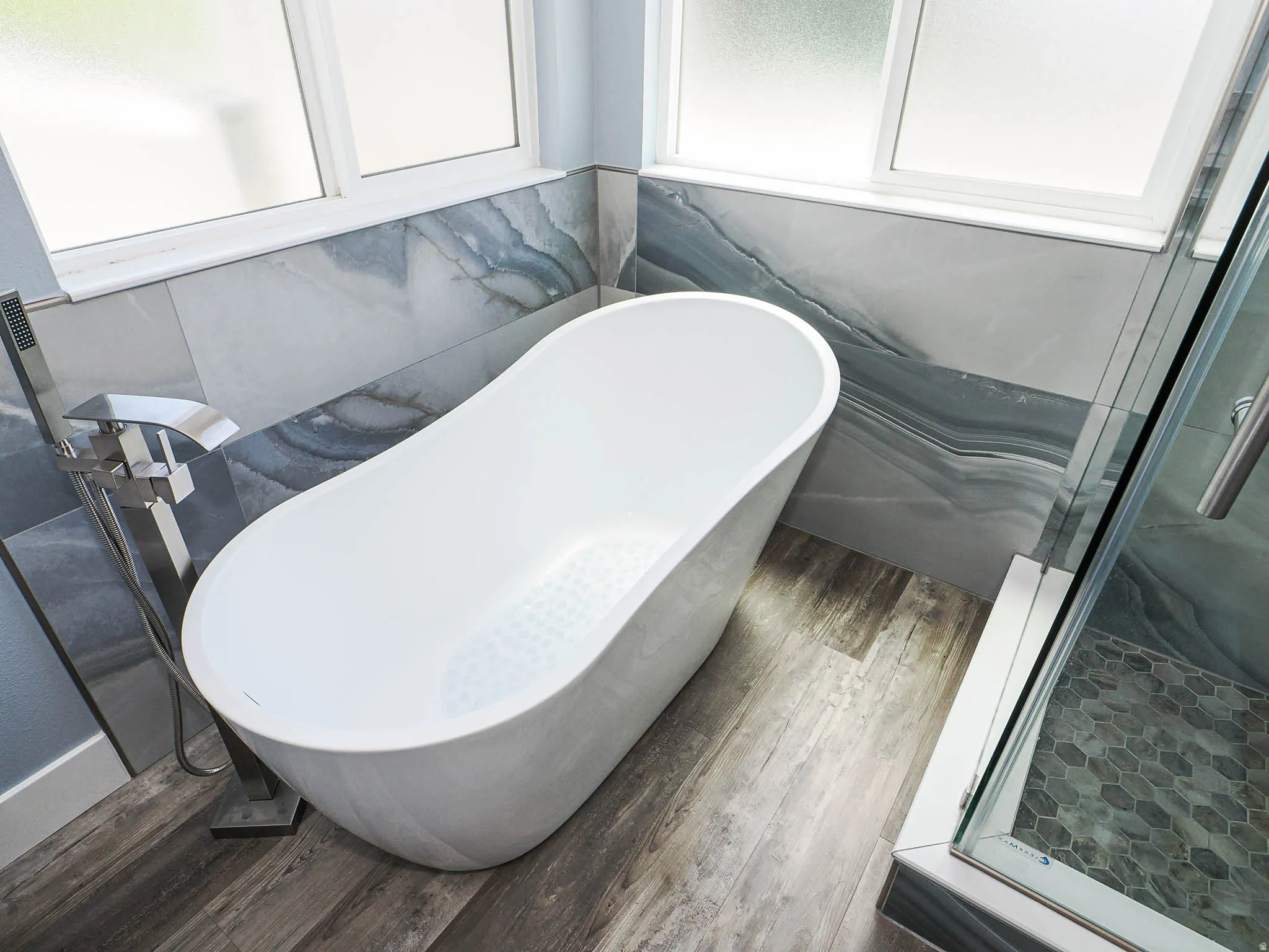 Freestanding soaking tub with a floor-mounted polished chrome faucet, set against a tiled accent wall