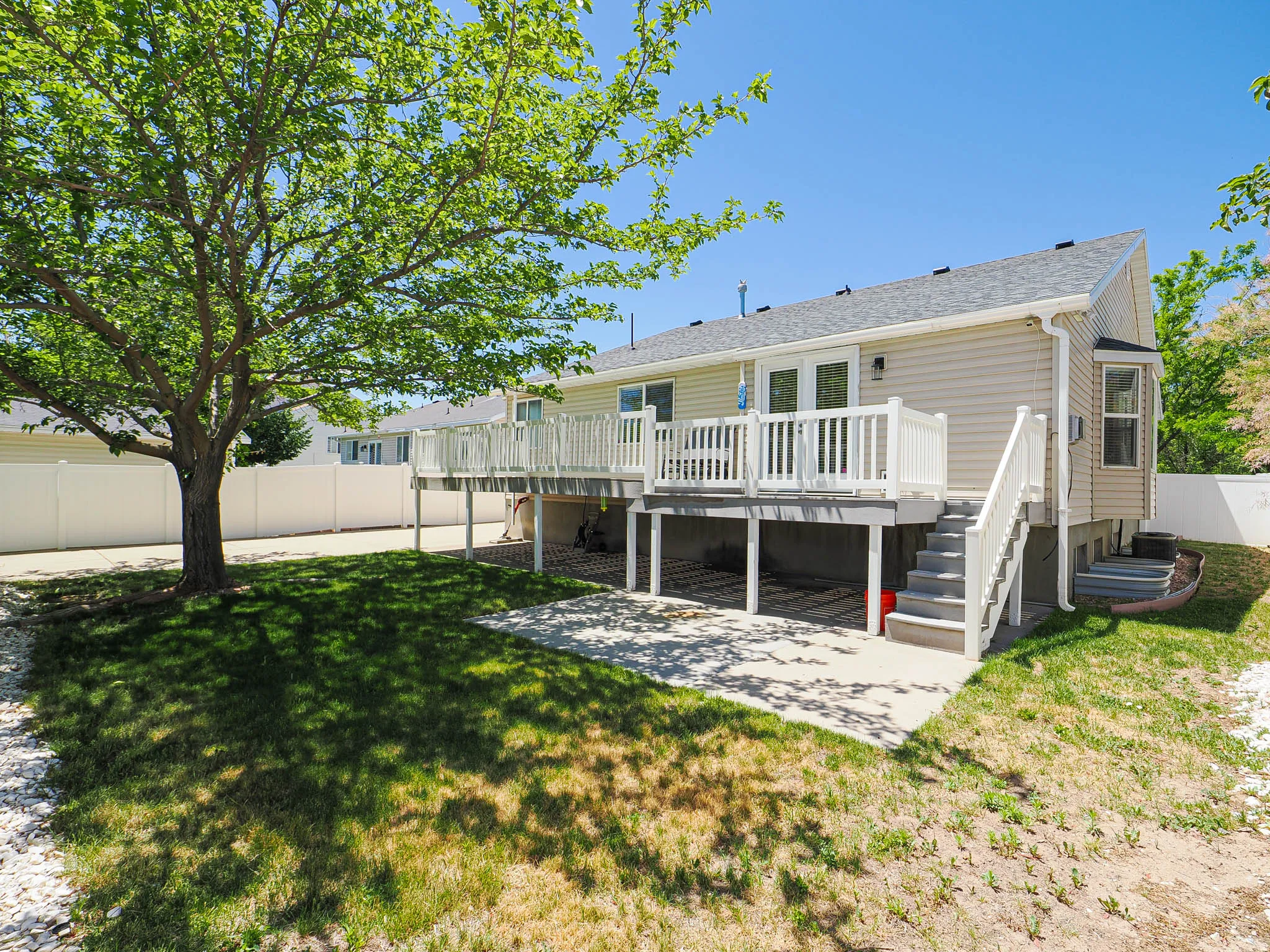 Rear exterior featuring a spacious elevated deck with white railings, a lower concrete patio, and a side staircase