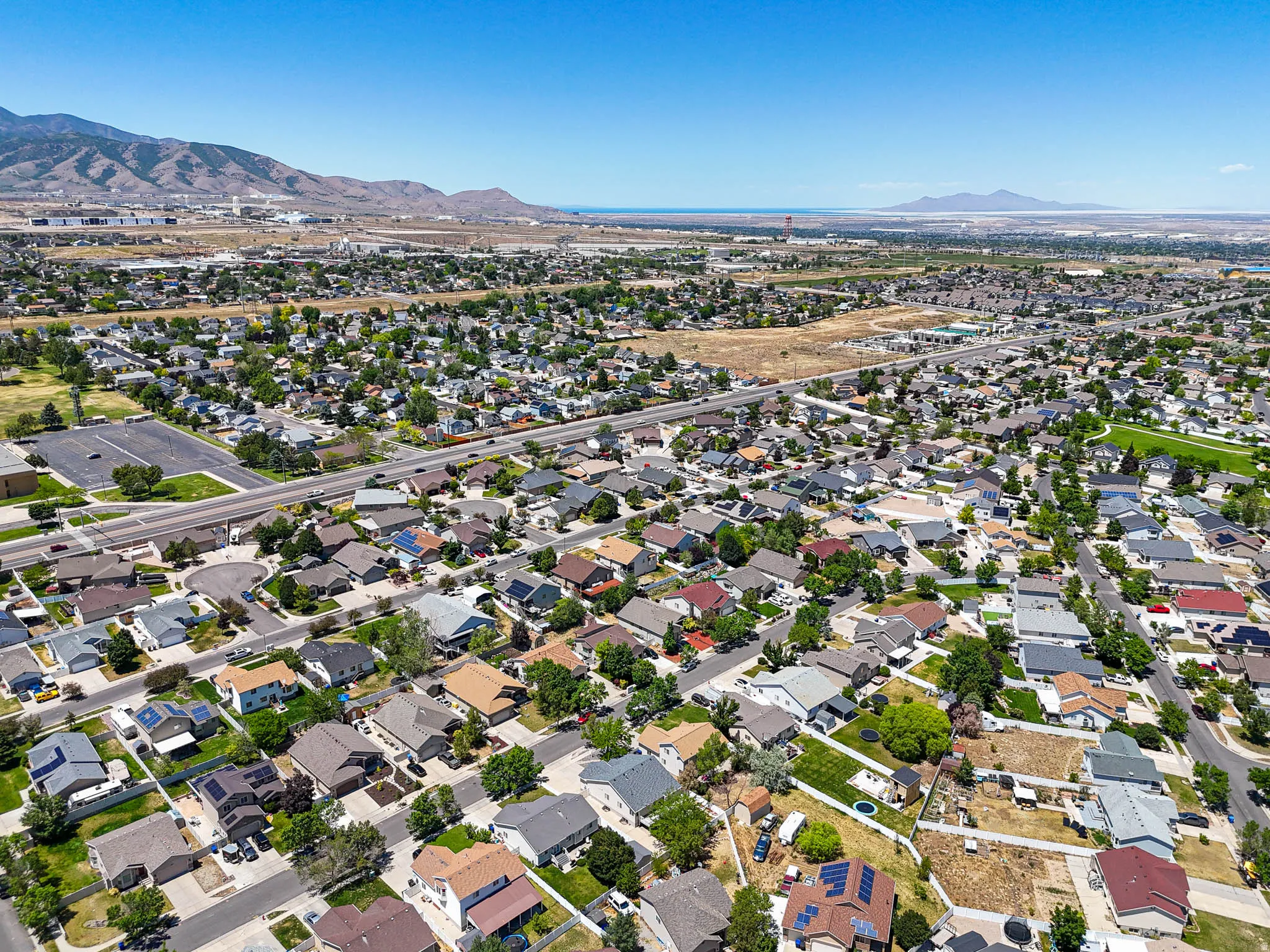Aerial perspective showcasing a residential neighborhood with diverse housing styles, mature trees, and mountainous terrain in the background