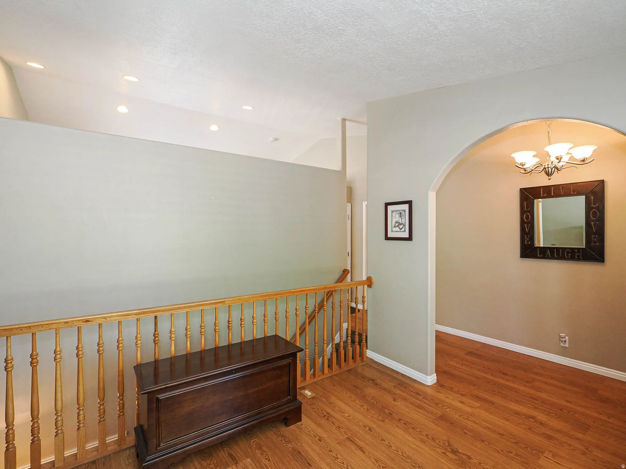 Upper-level landing featuring wood-finish flooring, a light wood railing, and an arched doorway