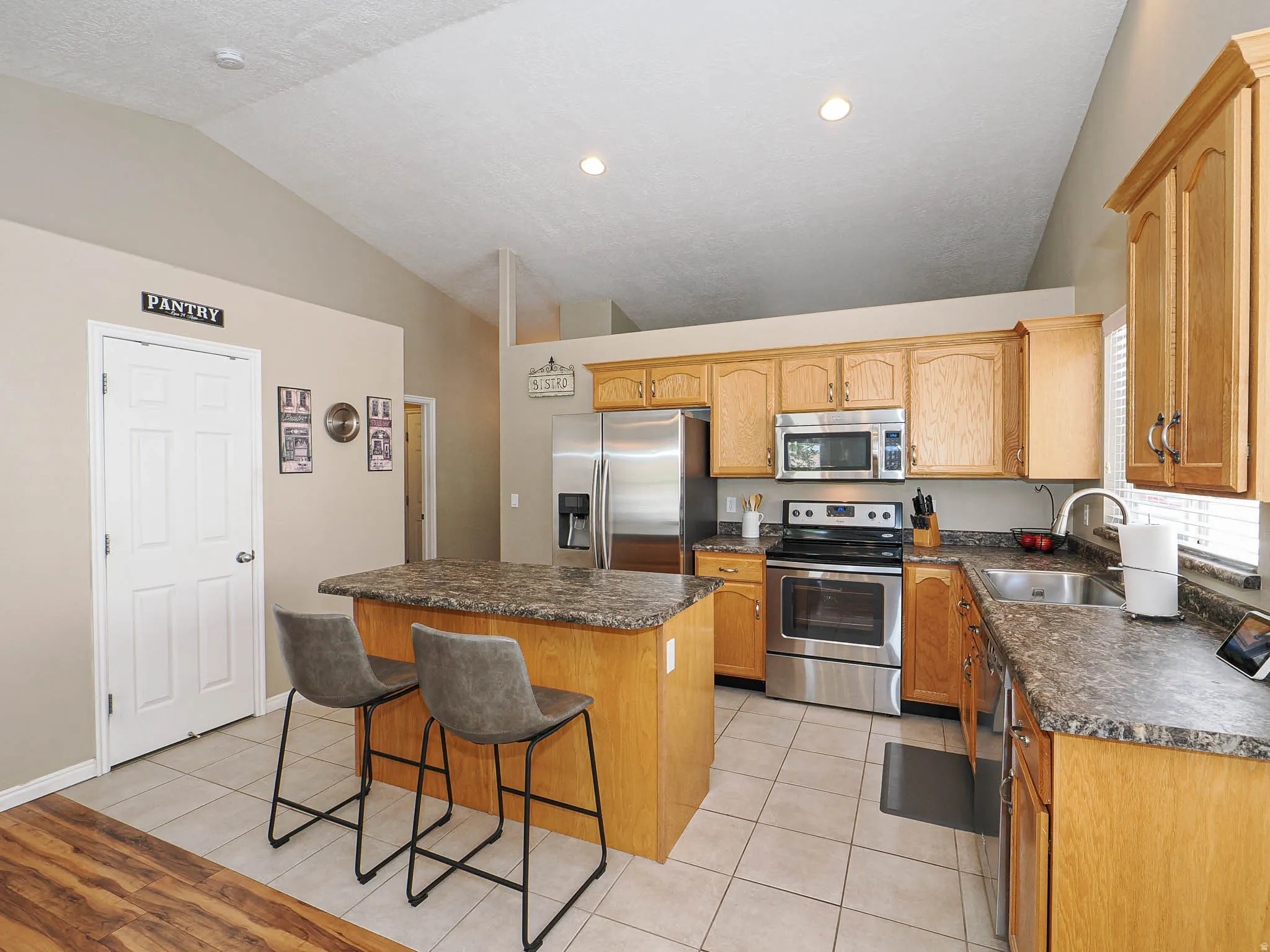 Vaulted ceiling kitchen featuring light wood cabinetry and a central island with a stone-finish countertop