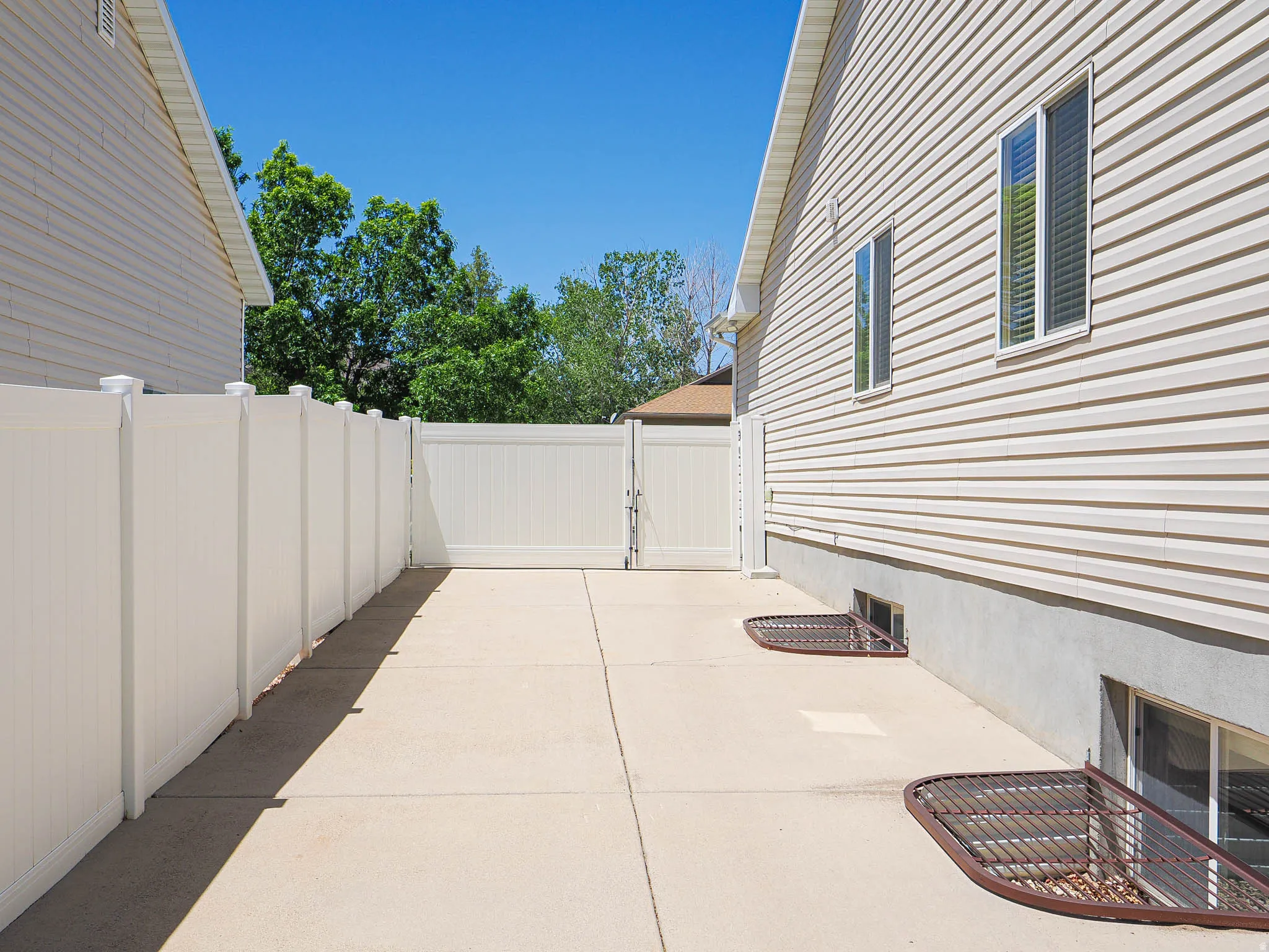Side yard featuring a concrete pad, white privacy fencing, and a double gate