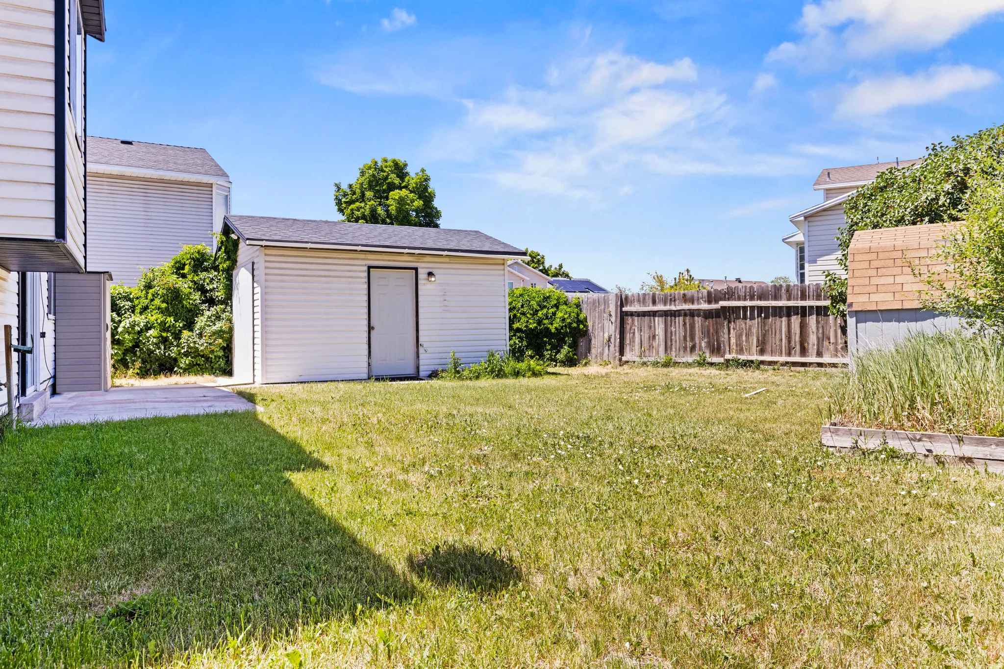 Spacious backyard featuring a detached storage shed with vinyl siding and a dark shingle roof, a wooden privacy fence, and concrete patio area