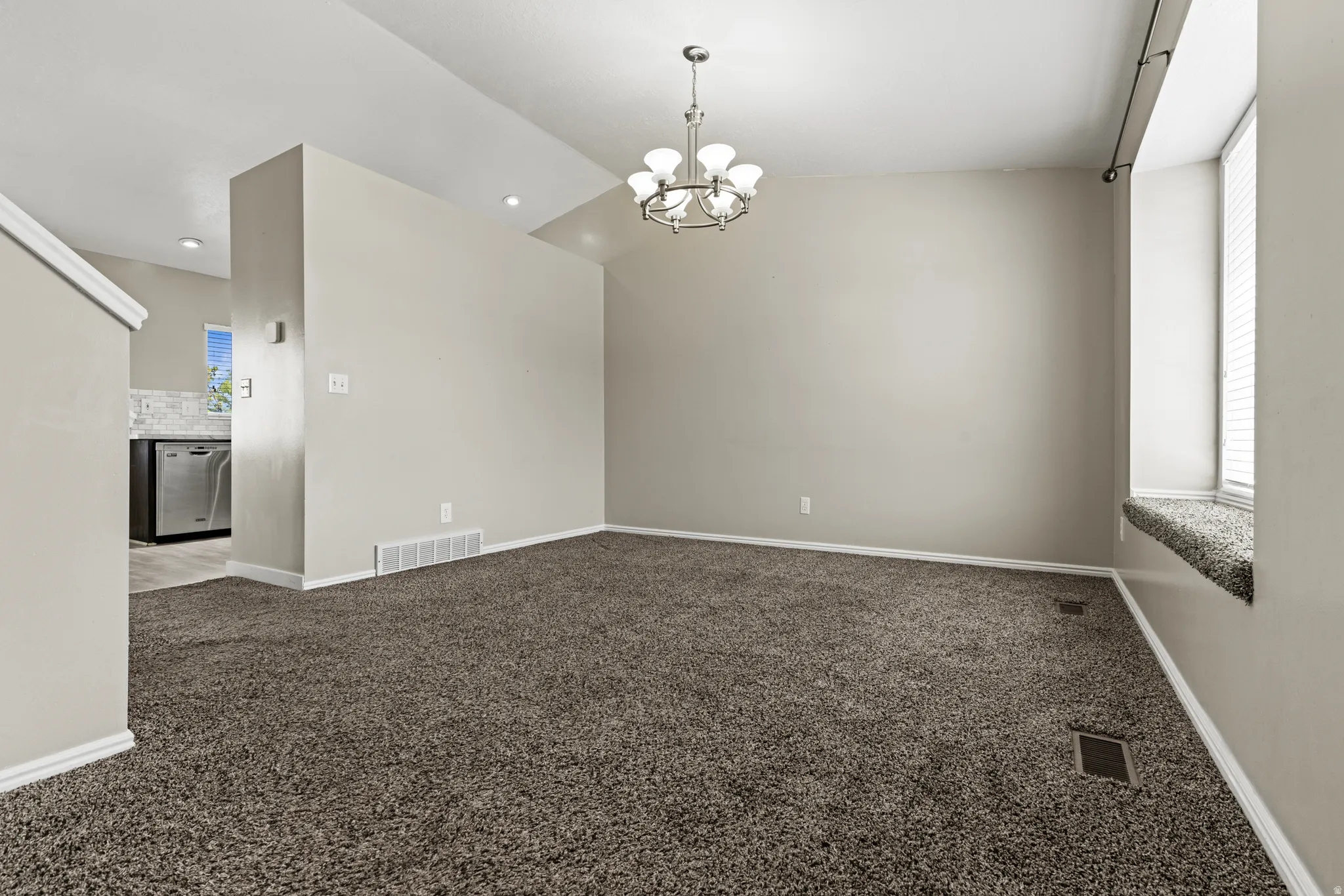 Spacious living area featuring neutral-toned carpeting, a contemporary chandelier, a window seat with blinds, and recessed lighting