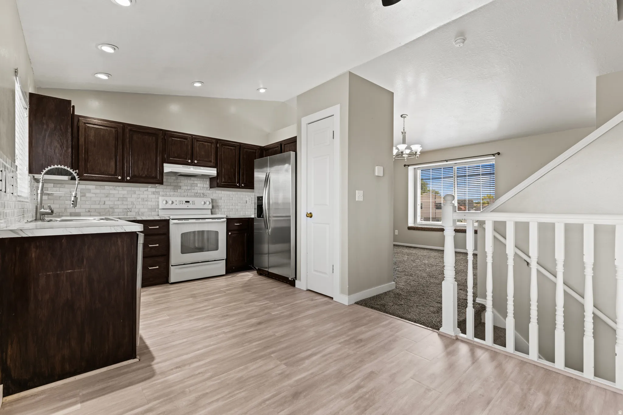 Kitchen featuring dark wood cabinetry, stainless steel refrigerator, white range, and a subway tile backsplash