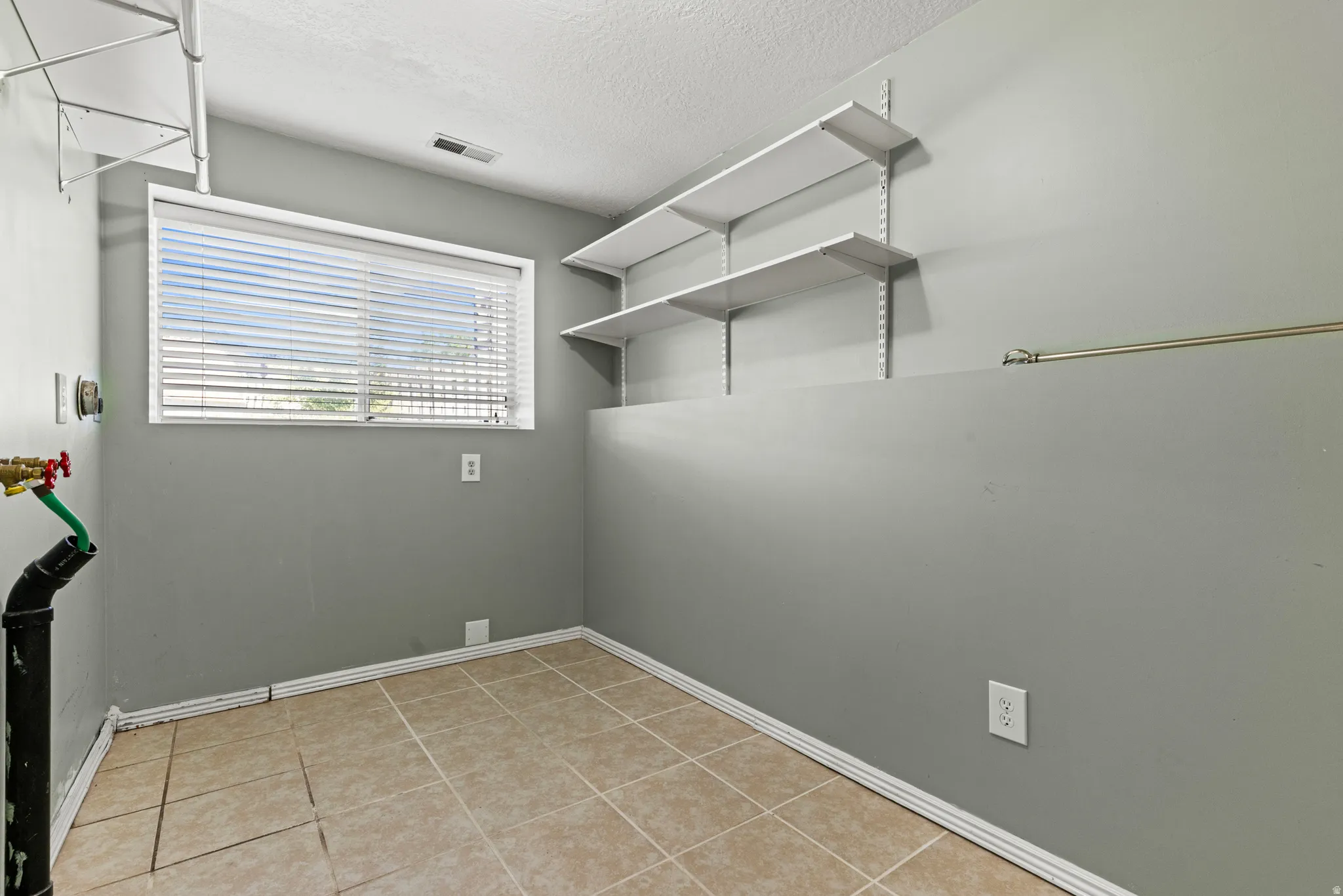 Utility room featuring light beige tile flooring, a horizontal window with blinds, and built-in wall shelving