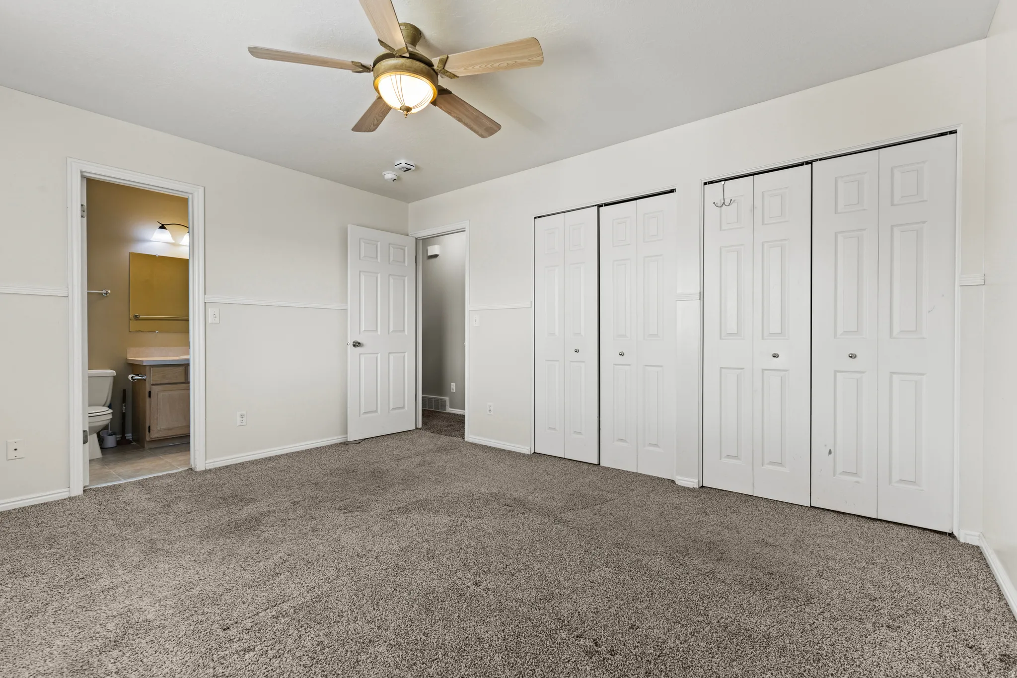 Spacious room featuring neutral carpet, white paneled doors, and a ceiling fan with integrated lighting