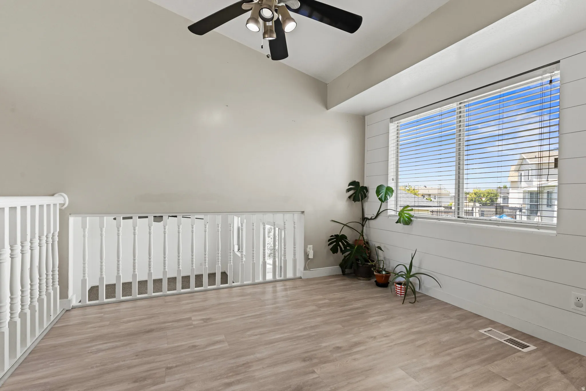 Spacious loft area featuring wood-finish flooring, a vaulted ceiling, and a ceiling fan with integrated lighting