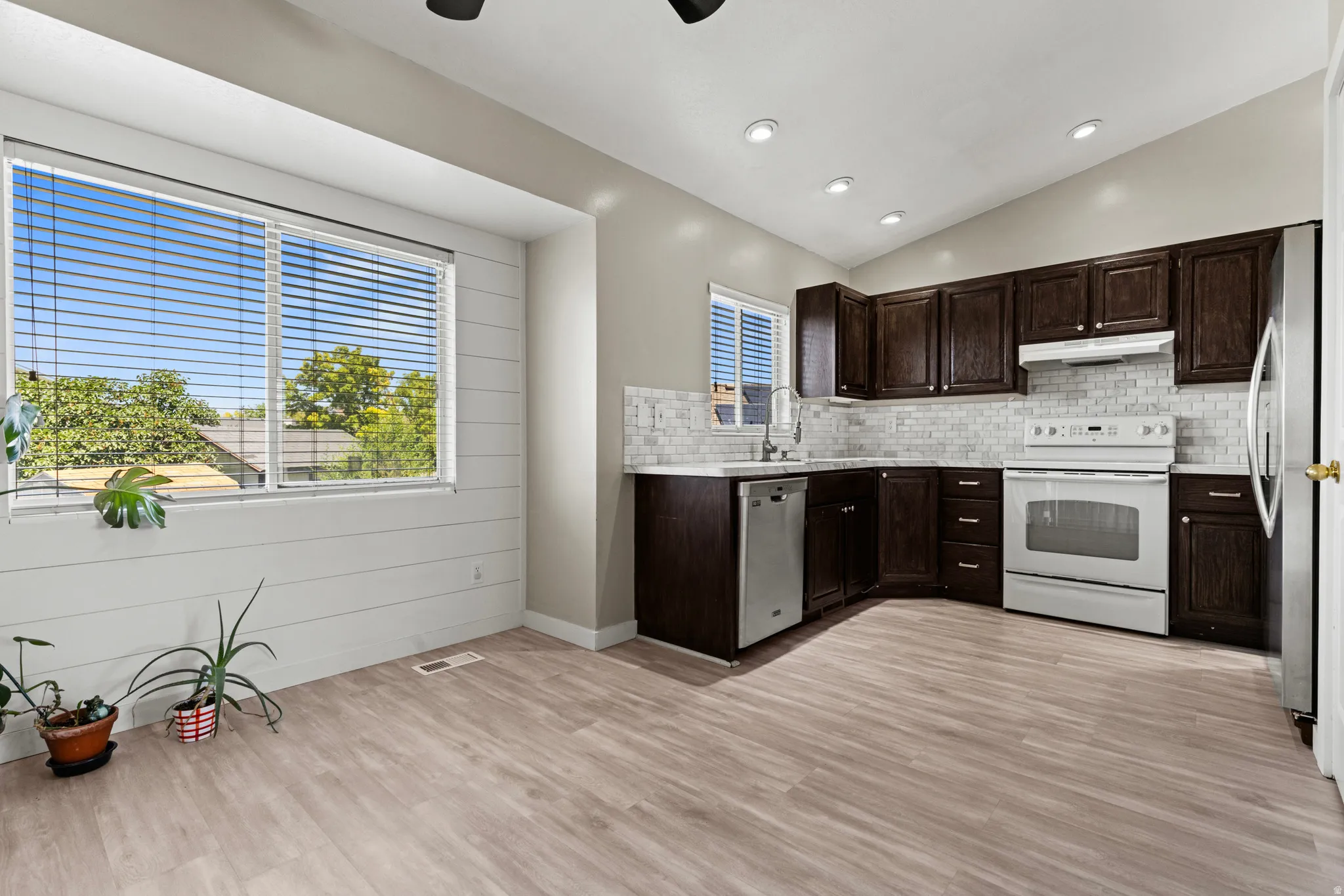 Kitchen featuring dark wood cabinetry, white subway tile backsplash, light wood-finish flooring, and a vaulted ceiling with recessed lighting