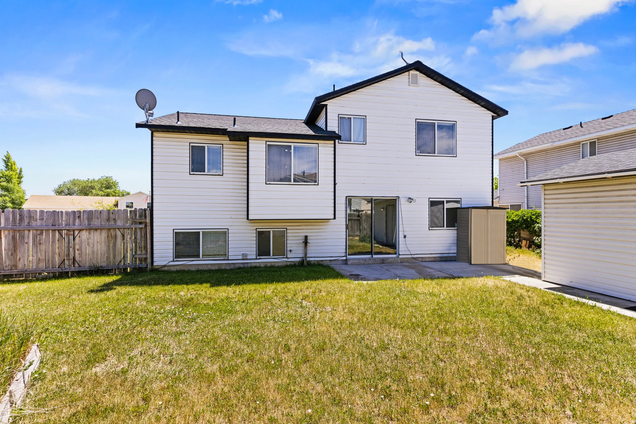 Rear exterior featuring white siding, a black shingled roof, sliding glass patio doors, and a concrete patio pad