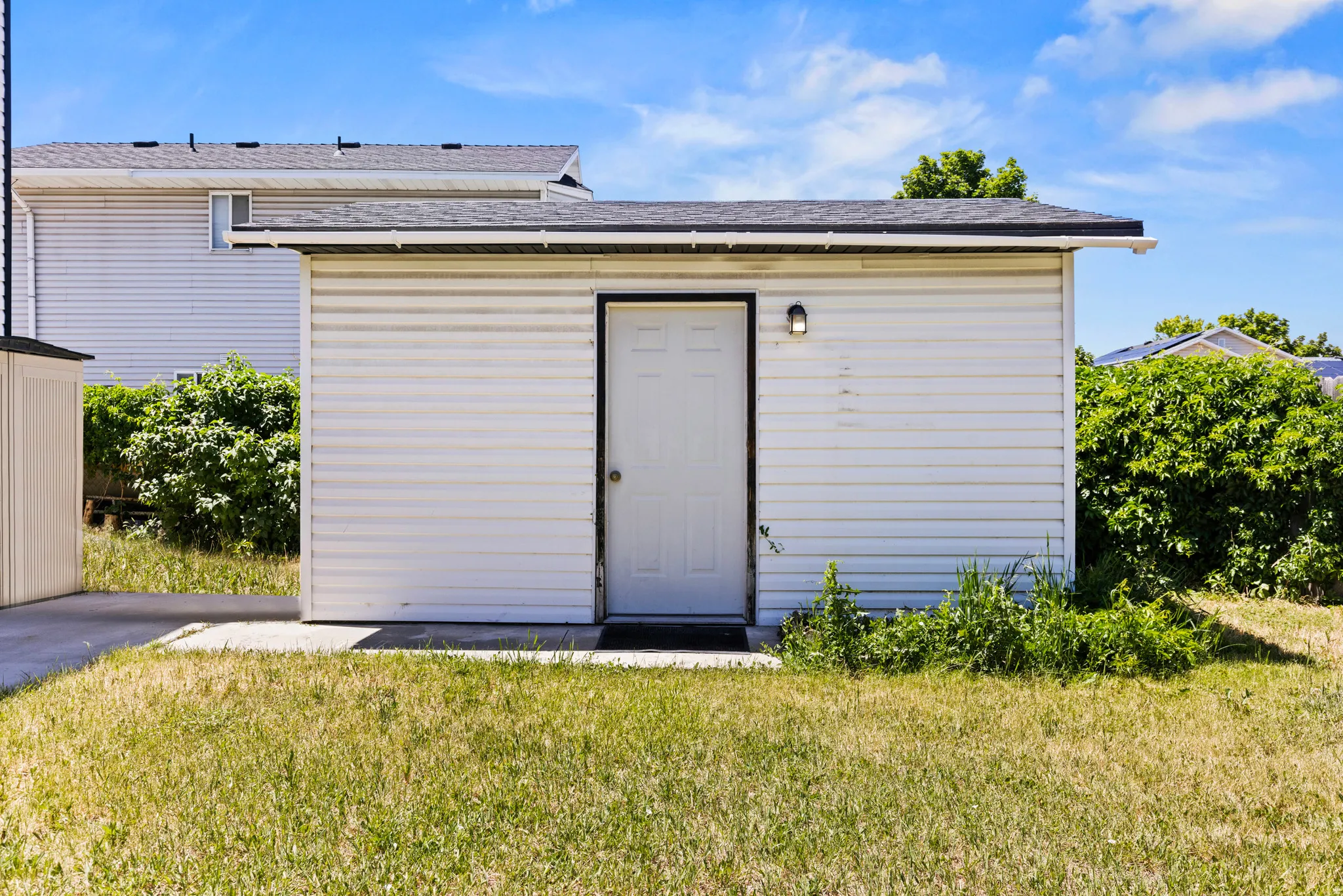Detached auxiliary building featuring white siding, a single entry door, and exterior lighting