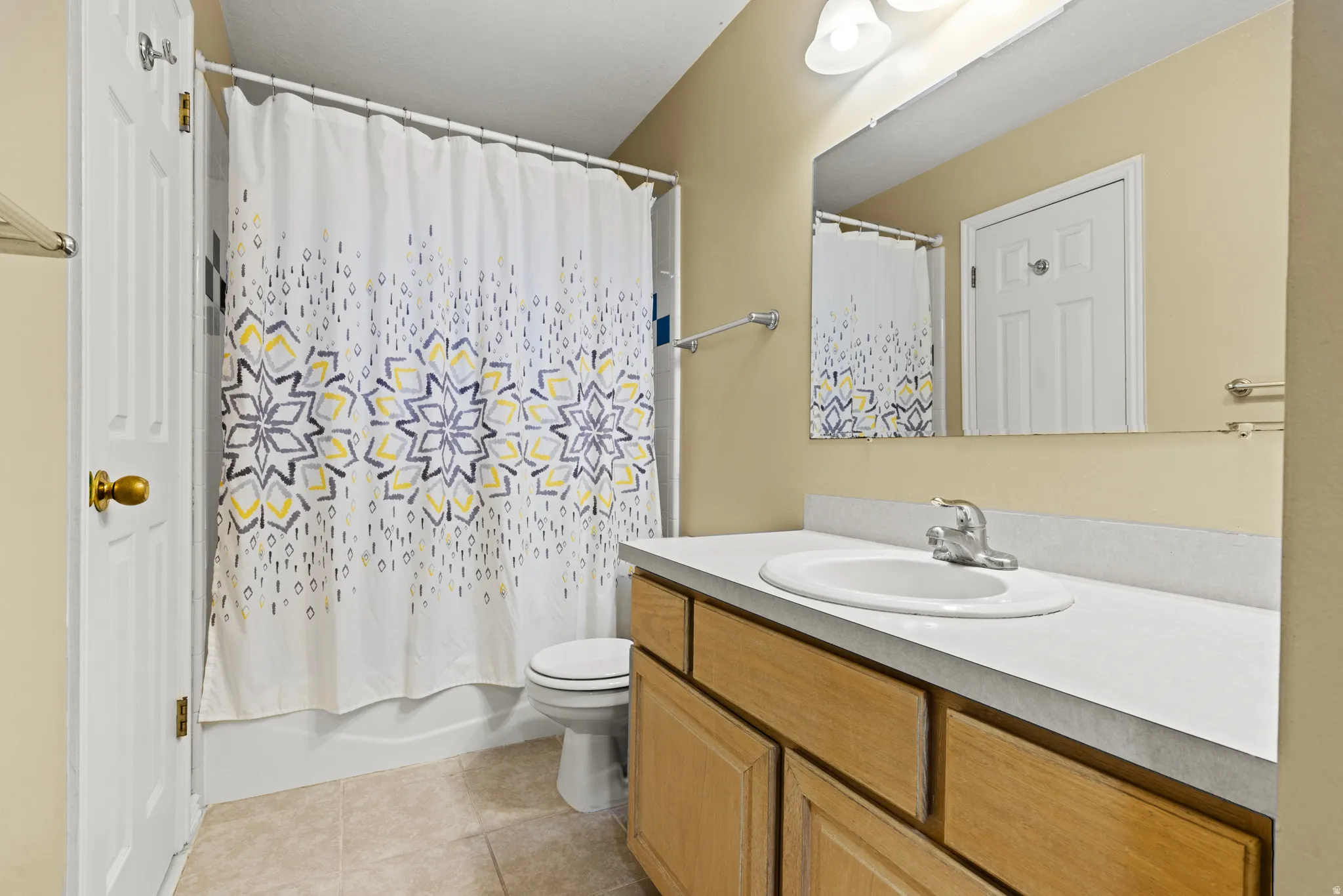 Full bathroom featuring a single vanity with wood-finish cabinetry, a white countertop with an integrated sink, a large wall-mounted mirror, and a shower-tub combination