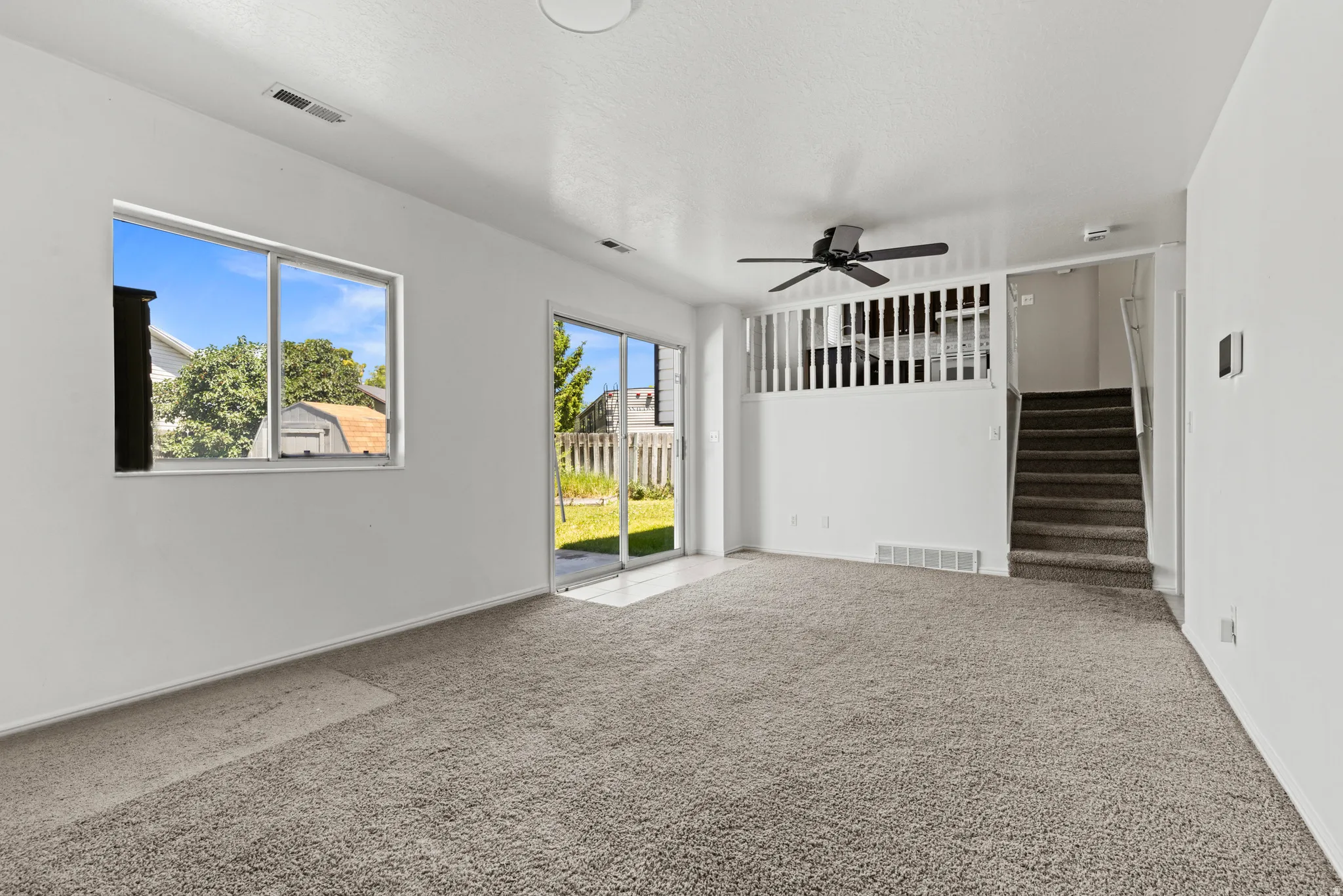 Carpeted living area featuring a ceiling fan, a large window, and a sliding glass door providing access to the exterior