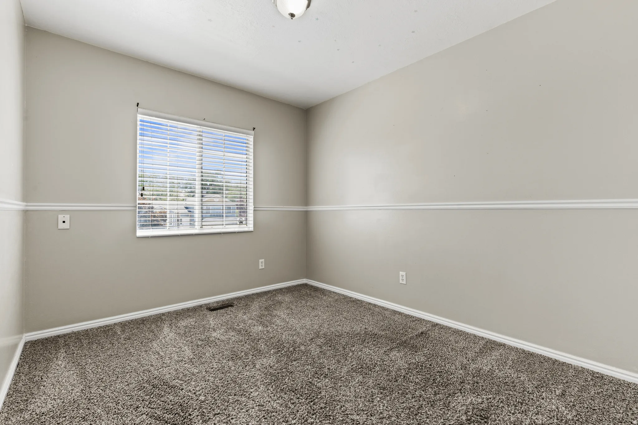 Carpeted room featuring a single window with horizontal blinds, neutral-toned walls, and a white ceiling