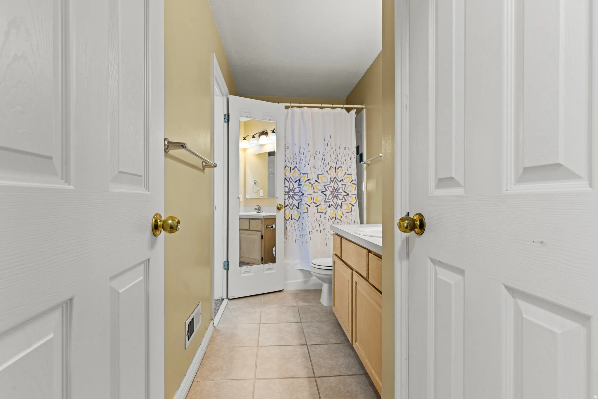 Bathroom featuring tile flooring, a light wood-finish vanity with a white countertop, and a shower with a patterned curtain