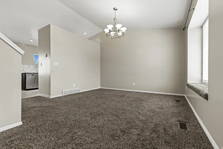 Spacious living area featuring neutral-toned carpeting, a contemporary chandelier, a window seat with blinds, and recessed lighting