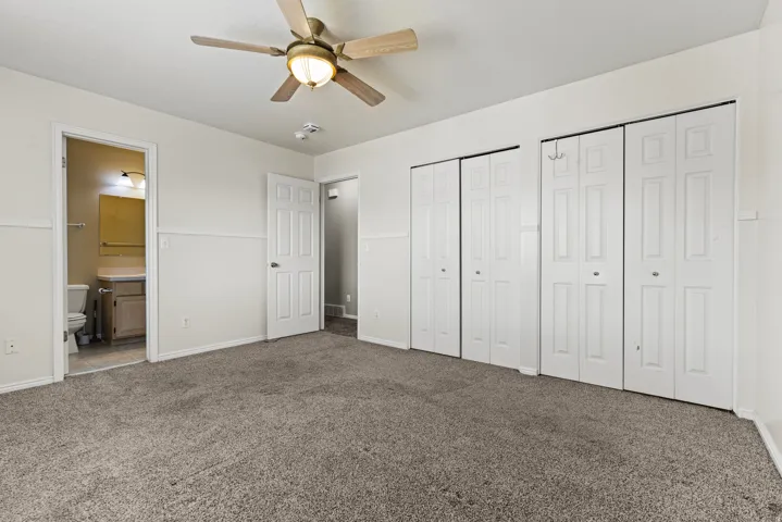Spacious room featuring neutral carpet, white paneled doors, and a ceiling fan with integrated lighting