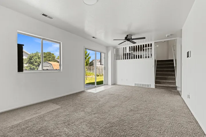 Carpeted living area featuring a ceiling fan, a large window, and a sliding glass door providing access to the exterior