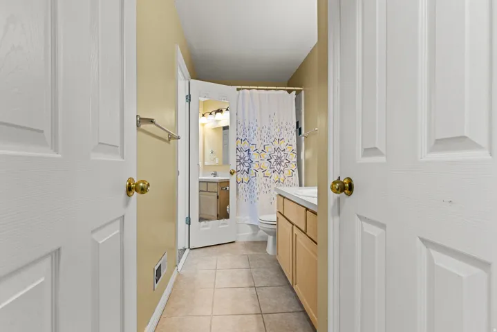Bathroom featuring tile flooring, a light wood-finish vanity with a white countertop, and a shower with a patterned curtain