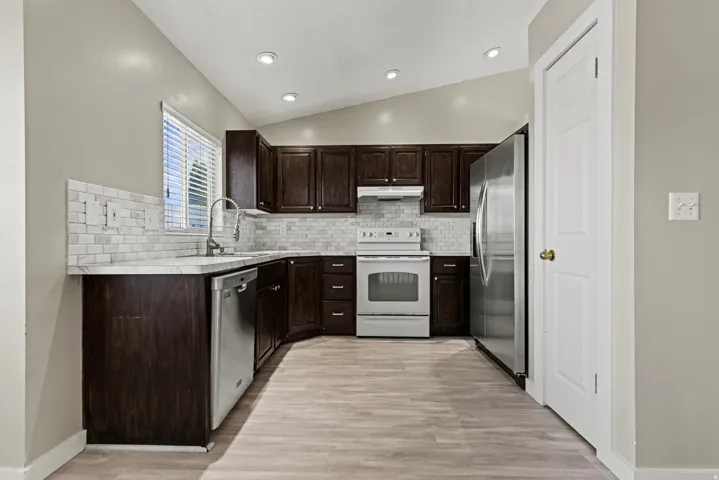 Kitchen featuring dark wood cabinetry, light-toned wood-finish flooring, white subway tile backsplash, stainless steel appliances, and recessed lighting
