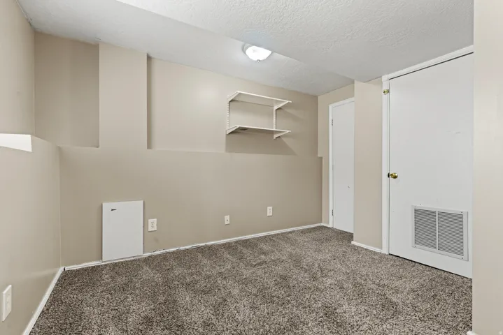 Carpeted room featuring neutral wall tones, built-in wall shelving, a flush-mount ceiling light fixture, and white trim