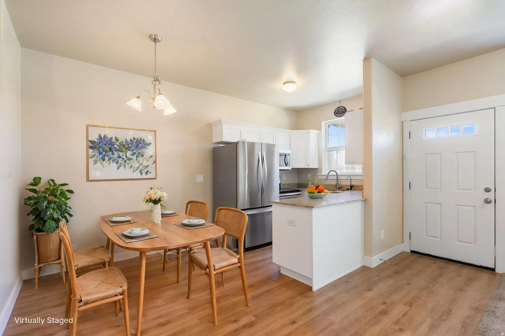 Bright kitchen and dining area featuring wood-finish flooring, white cabinetry, stainless steel appliances, and a granite countertop
