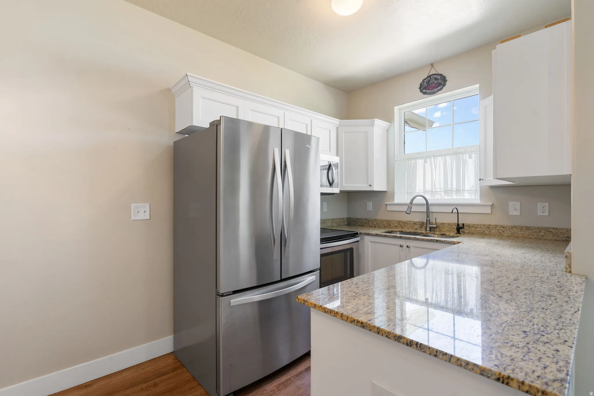Kitchen featuring white cabinetry, stainless steel appliances, granite countertop, and wood-finish flooring