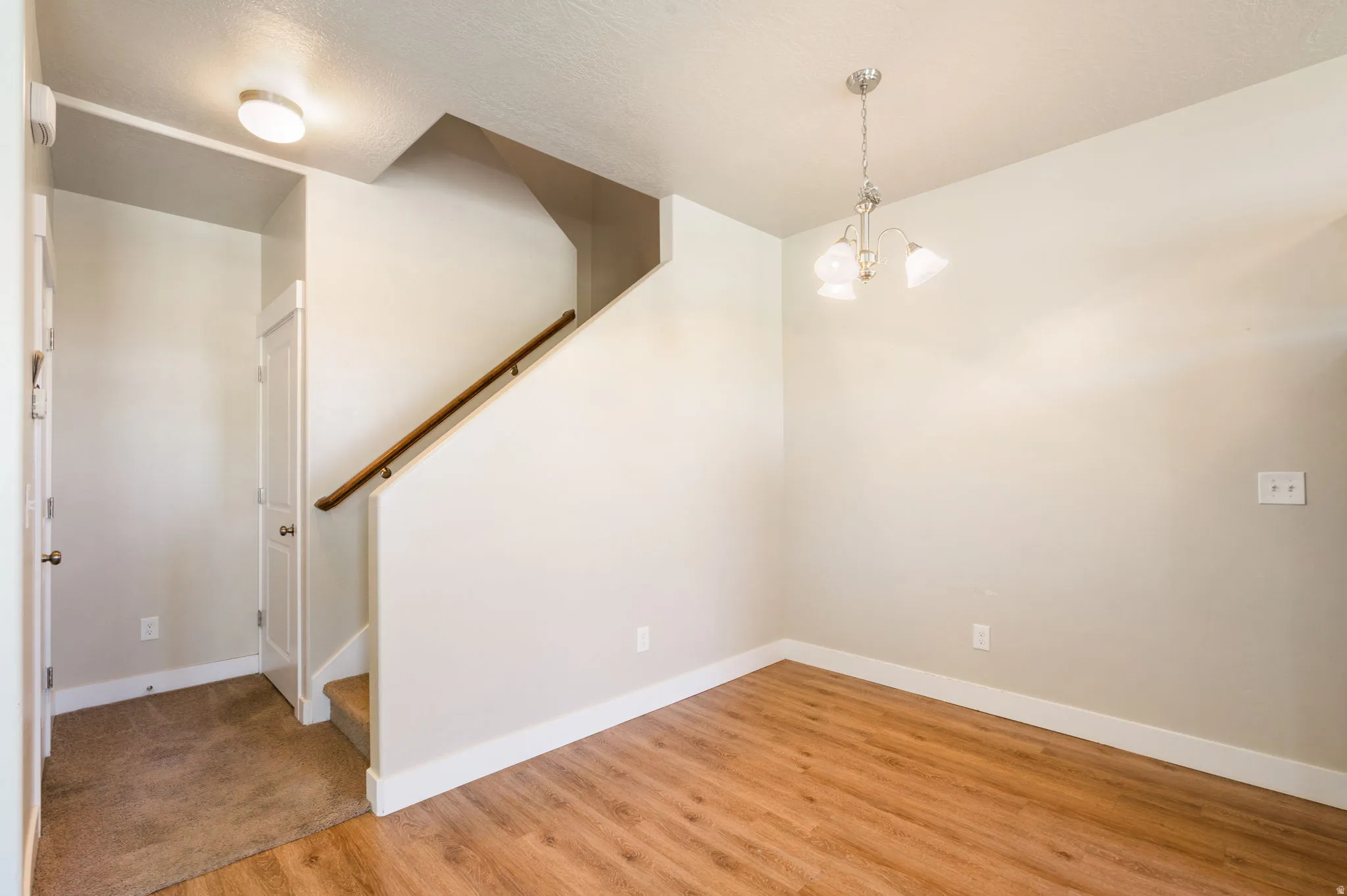 Open concept space featuring wood-finish flooring, a contemporary chandelier, and a carpeted entryway with a built-in closet
