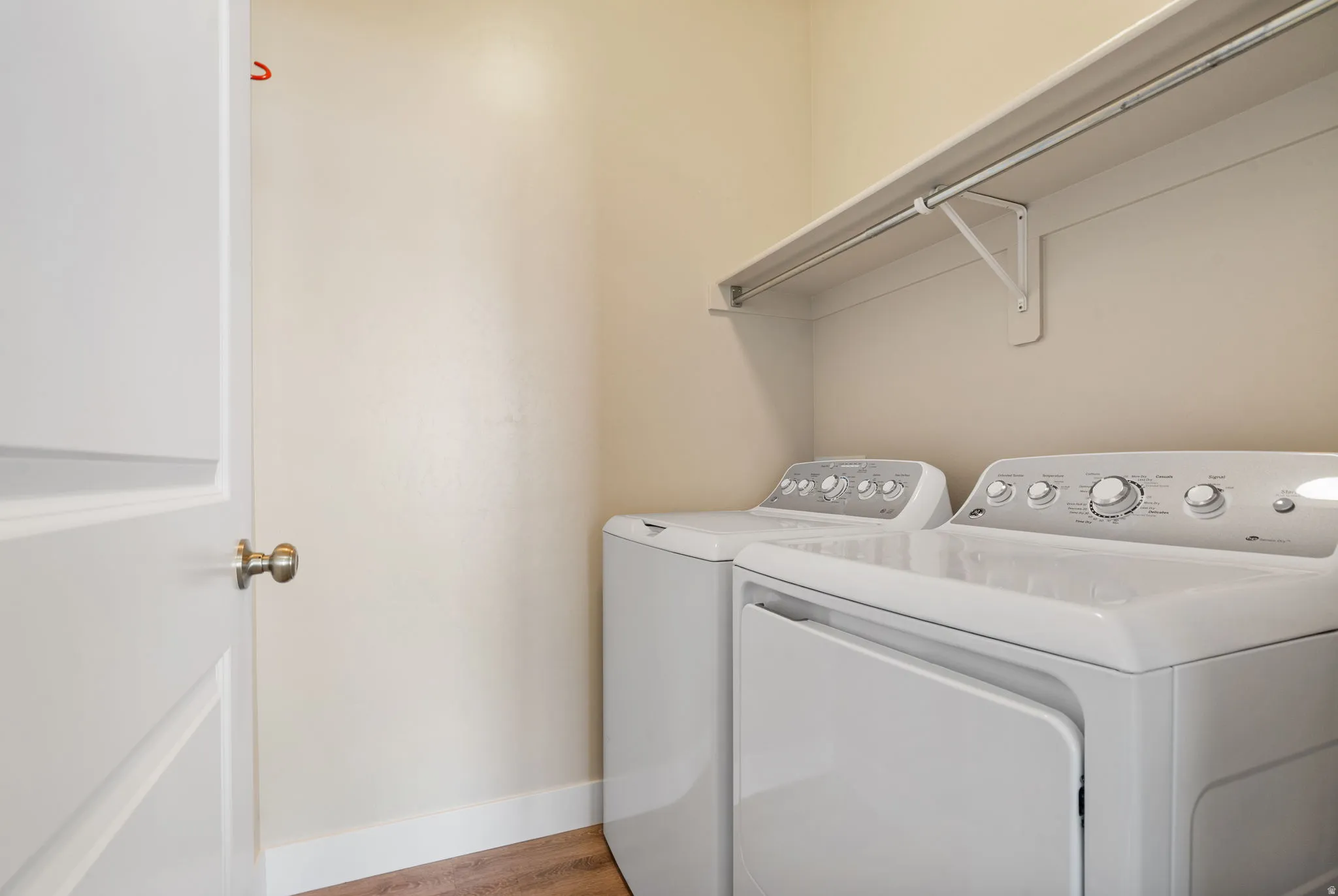 Laundry area featuring wood-finish flooring, light-toned walls, and a built-in storage shelf with hanging rod