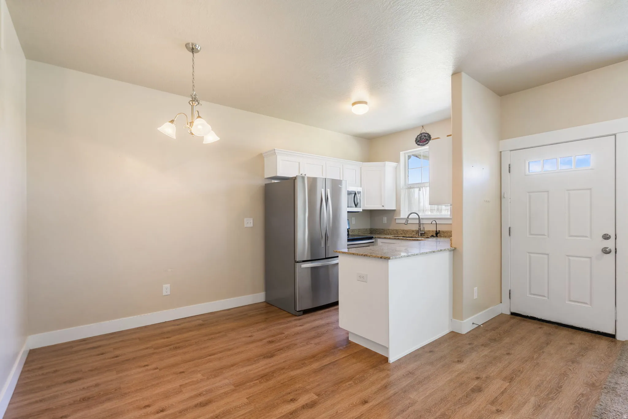 Open-concept living area featuring wood-finish flooring, granite countertop, and a three-light chandelier