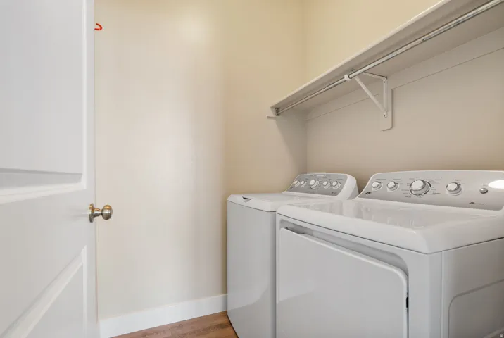 Laundry area featuring wood-finish flooring, light-toned walls, and a built-in storage shelf with hanging rod