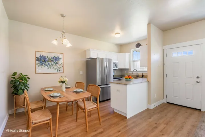 Bright kitchen and dining area featuring wood-finish flooring, white cabinetry, stainless steel appliances, and a granite countertop