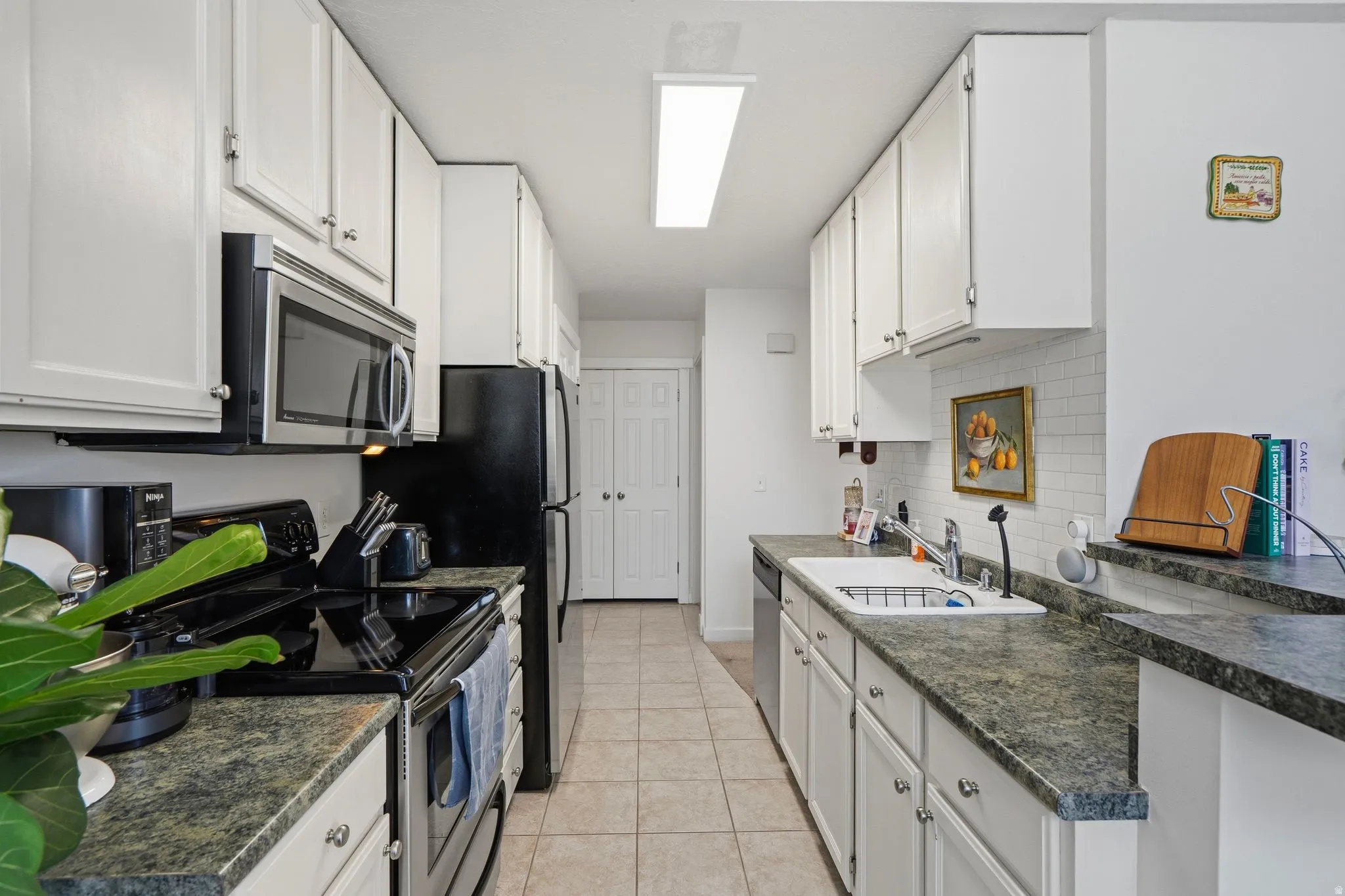 Galley kitchen featuring white cabinetry, dark speckled countertops, and a white subway tile backsplash