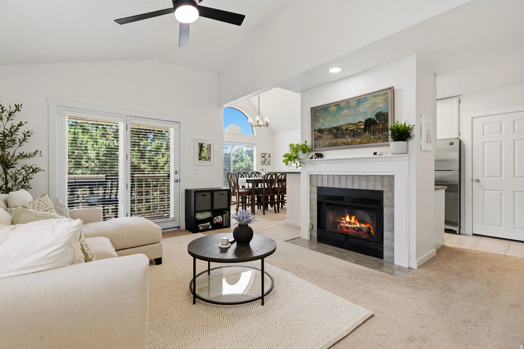 Living area featuring vaulted ceilings, a ceiling fan, a fireplace with a tile surround and mantle, and sliding glass doors to outdoor space