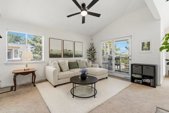 Vaulted ceiling living area featuring a ceiling fan, wall-to-wall carpeting, and a sliding glass door to an exterior balcony