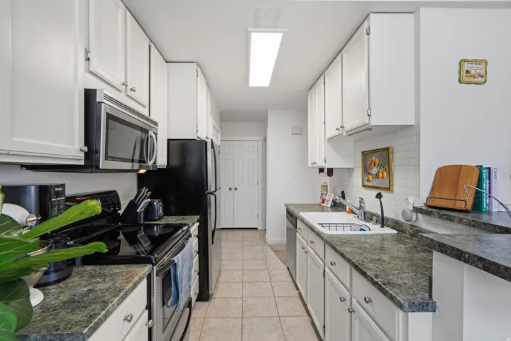 Galley kitchen featuring white cabinetry, dark speckled countertops, and a white subway tile backsplash