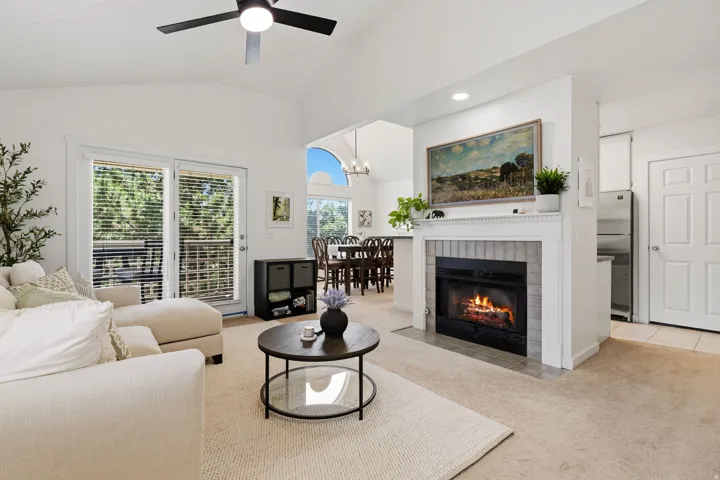 Living area featuring vaulted ceilings, a ceiling fan, a fireplace with a tile surround and mantle, and sliding glass doors to outdoor space