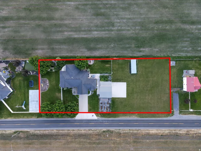 Expansive property featuring a single-family residence with a dark shingled roof, a paved driveway, and established landscaping