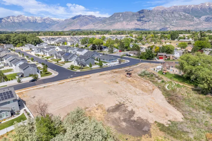 Expansive undeveloped land parcel featuring a clear, level building area, direct street access, established surrounding residential properties, and distant mountain vistas