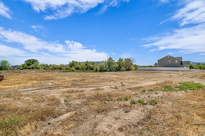 Expansive land parcel featuring a cleared, level terrain, partial fencing, and distant residential structures