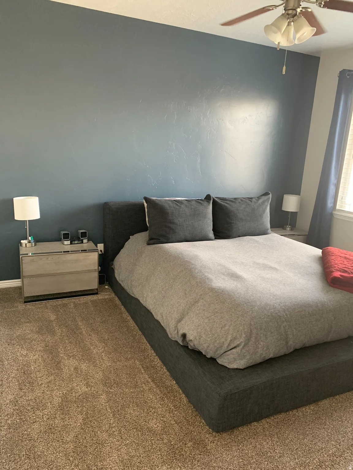 Bedroom featuring a prominent accent wall, textured carpeting, and a ceiling fan with light fixture
