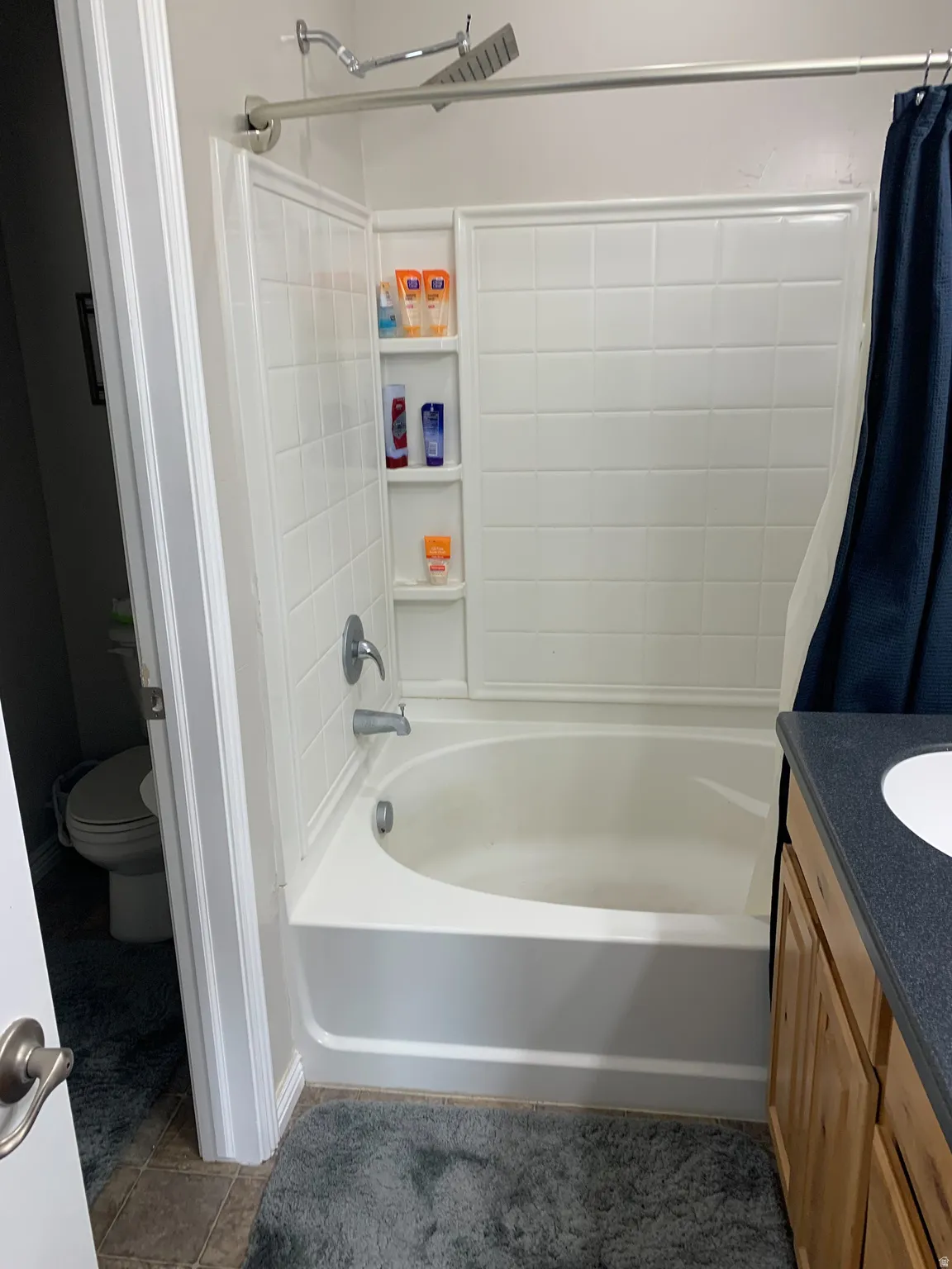 Bathtub and shower combination featuring a white tiled surround, built-in shelving, and a chrome rainfall showerhead