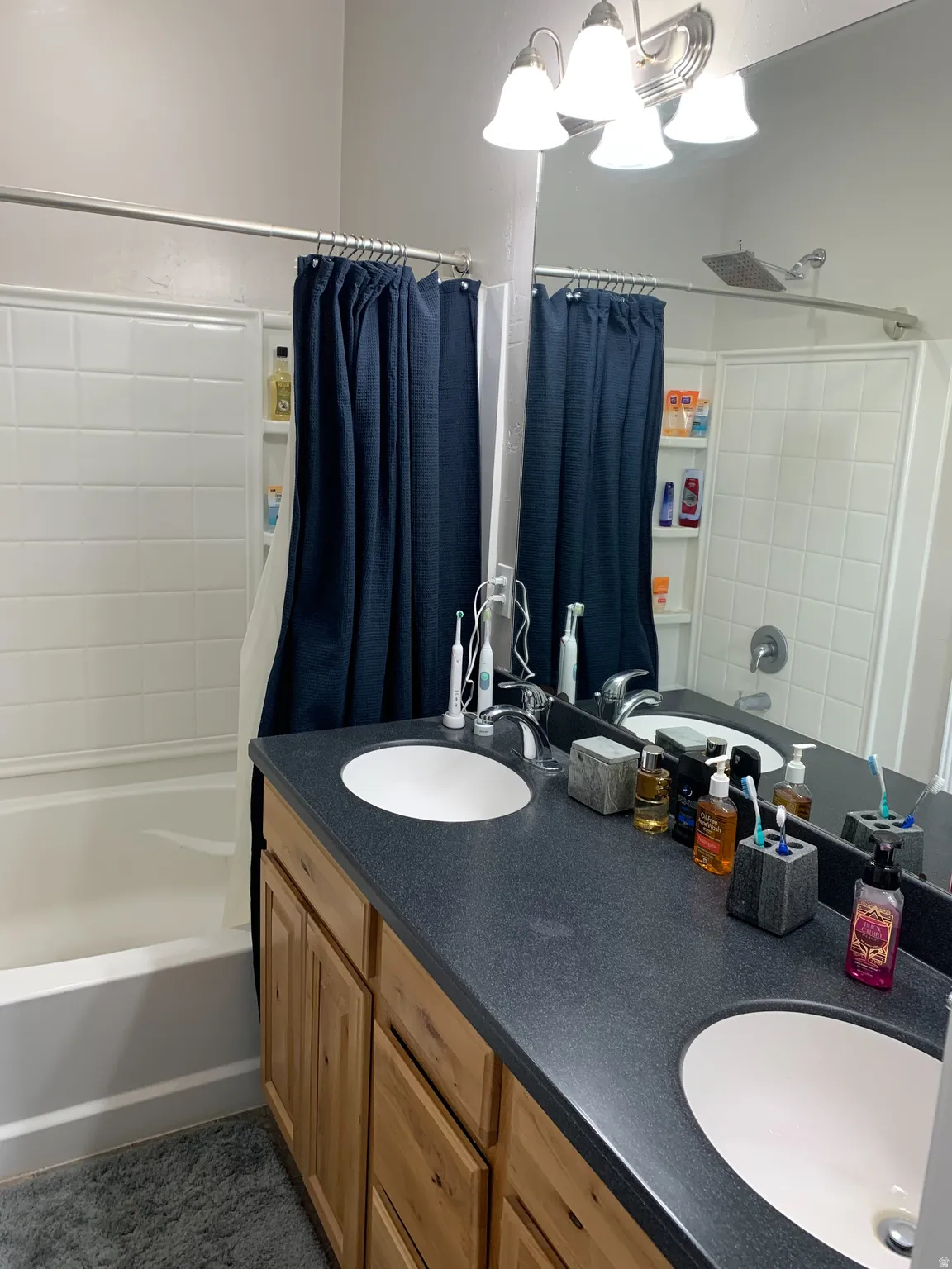 Bathroom featuring a dual vanity with light wood-finish cabinetry, a dark speckled countertop, and two undermount sinks