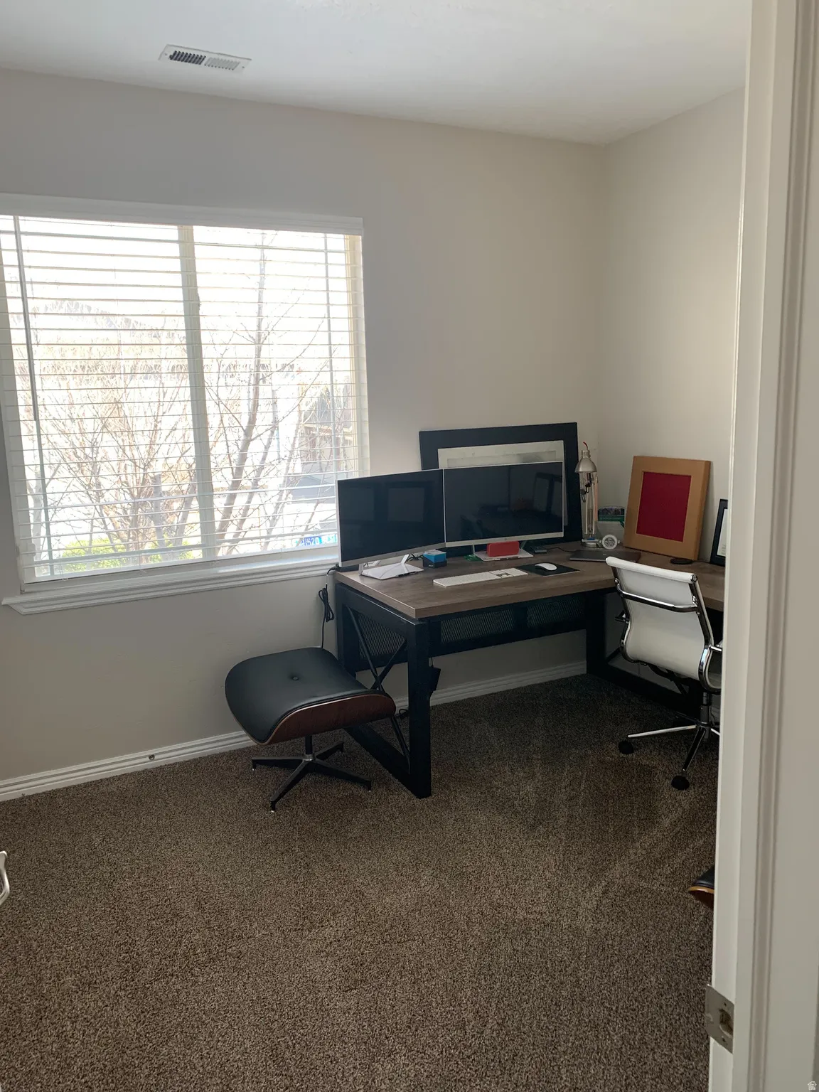 Room featuring a large window with horizontal blinds, neutral wall paint, and brown carpeting