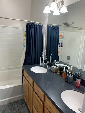 Bathroom featuring a dual vanity with light wood-finish cabinetry, a dark speckled countertop, and two undermount sinks