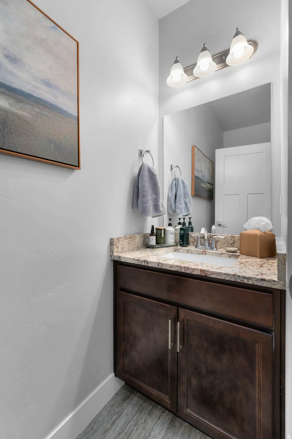 Bathroom vanity featuring a granite countertop, undermount sink, dark wood cabinetry, and brushed nickel hardware