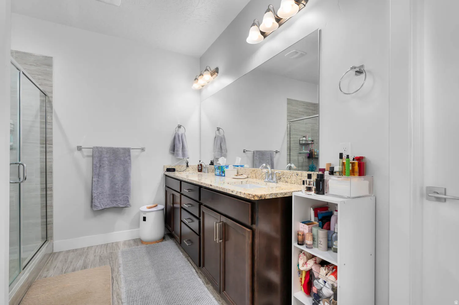 Bathroom featuring a dual vanity with a speckled countertop, dark wood-finish cabinetry, and an oversized mirror
