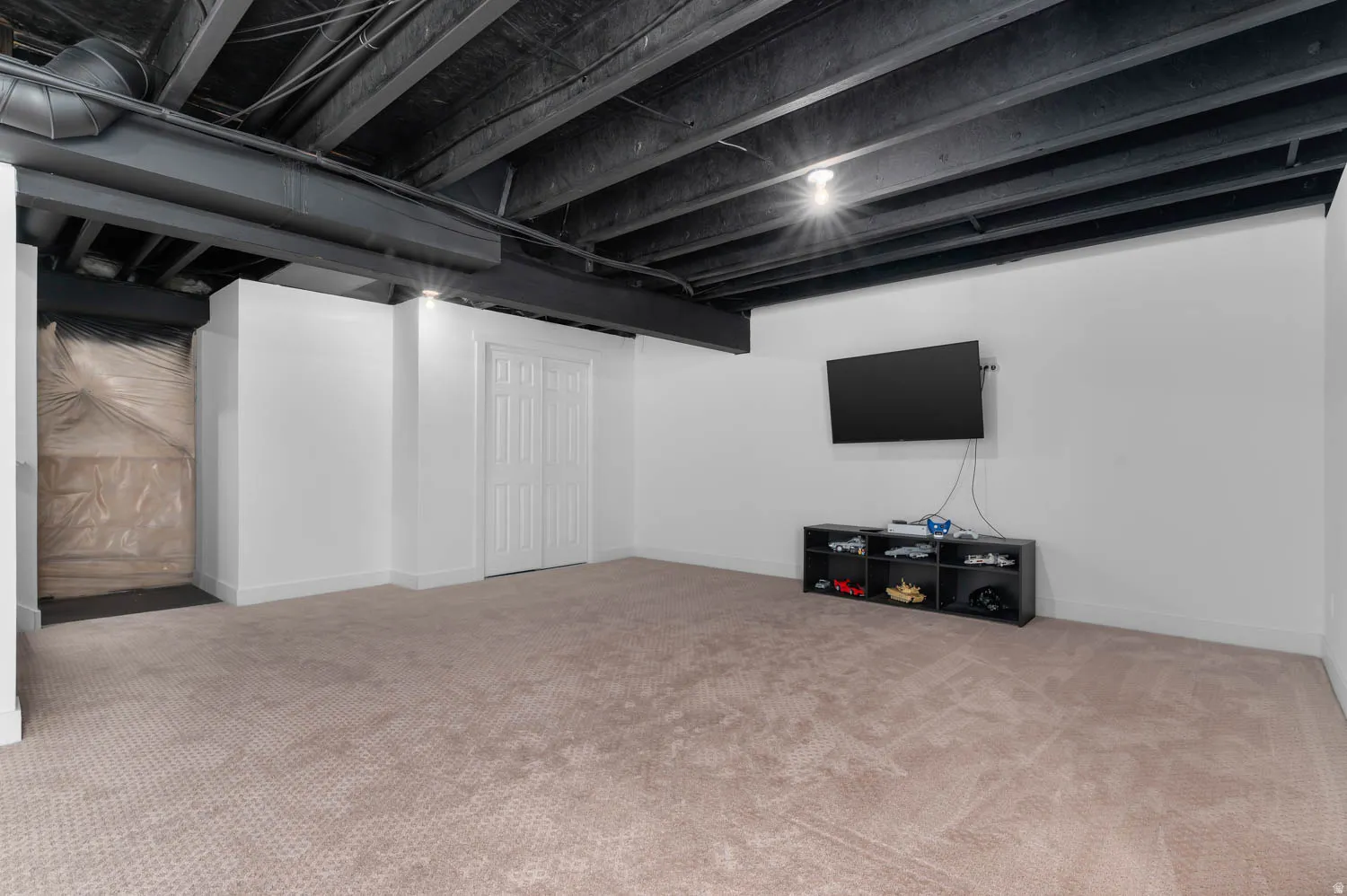 Finished basement space featuring plush carpeting, white painted walls, and a painted exposed ceiling