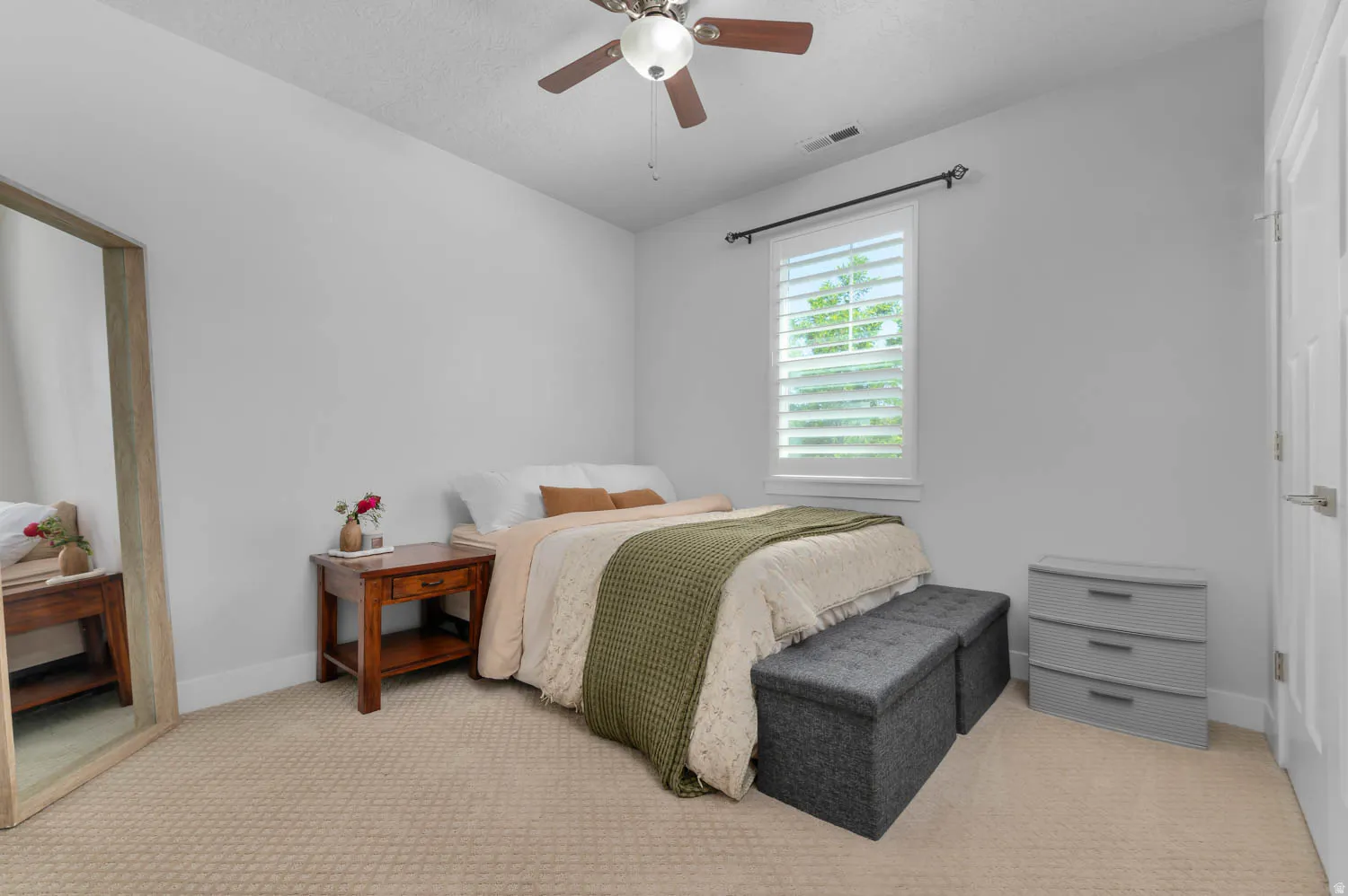 Bedroom featuring neutral wall colors, textured carpeting, a window with white plantation shutters, and a ceiling fan with integrated lighting