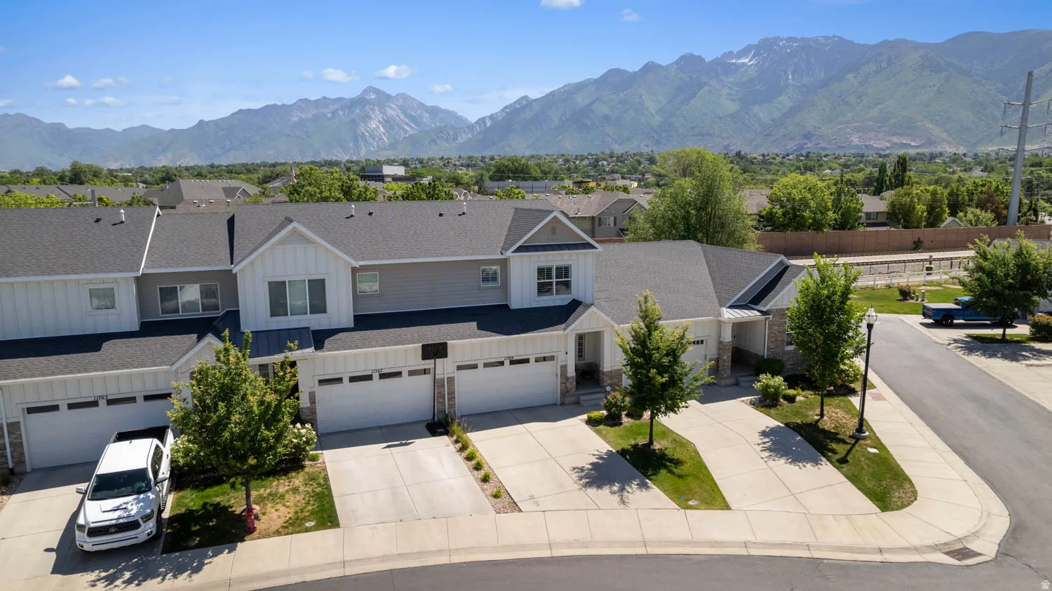 Townhome community with a mountain backdrop, featuring a gray and white exterior with stone accents, attached garages, and individual driveway parking